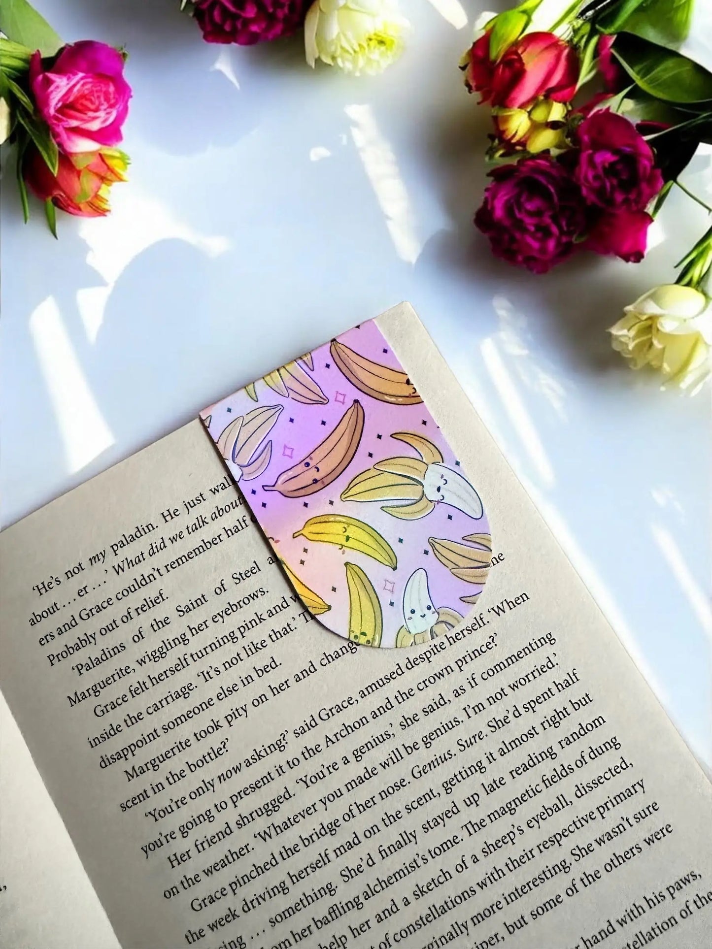 Cute smiling Banana Bunch magnetic bookmark holding the page in an open book by Enchanted Bookcase