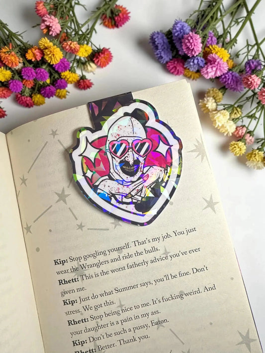Horror clown with heart sunglasses holographic magnetic bookmark placed in an open book by Enchanted Bookcase
