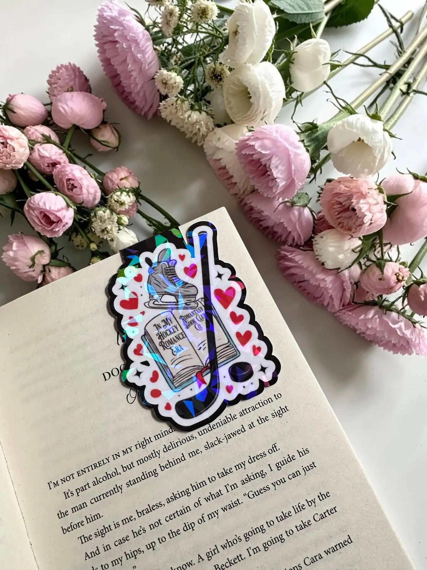In My Hockey Romance Era hockey skate, book, and stick holographic magnetic bookmark in an open book by Enchanted Bookcase