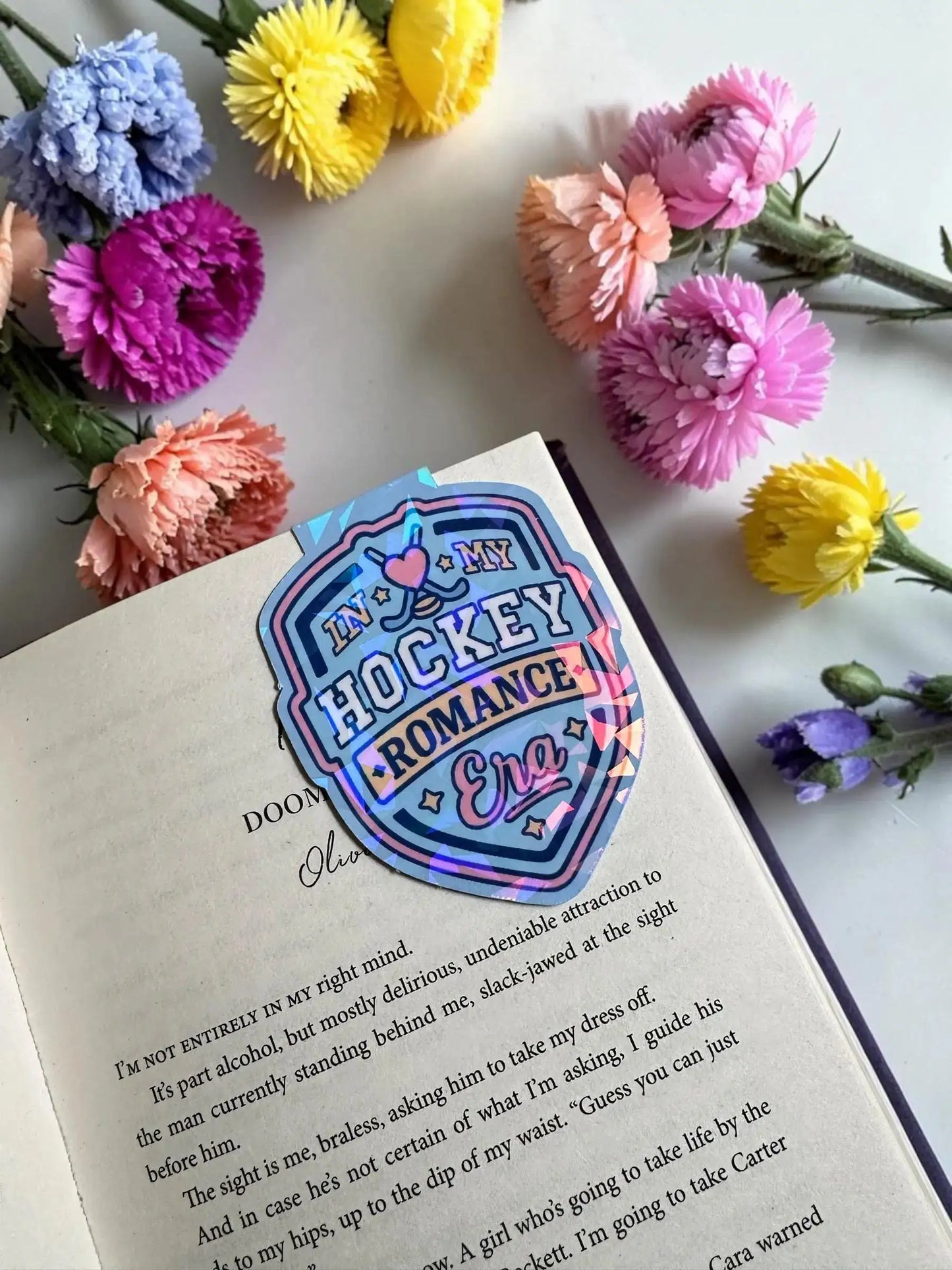 In My Hockey Romance Era blue shield holographic magnetic bookmark placed in an open book by Enchanted Bookcase