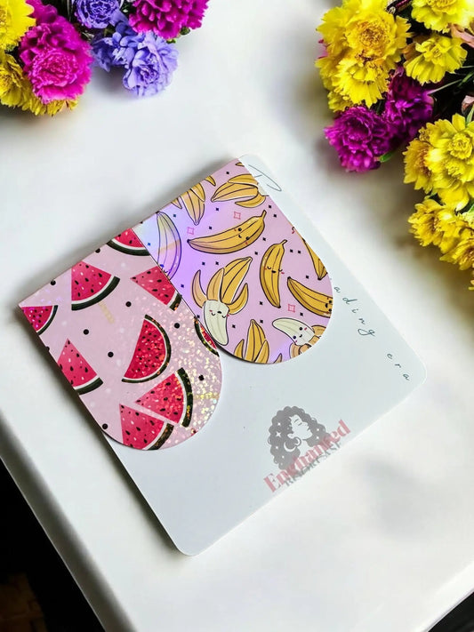 Watermelon Sparkle and Banana Bunch handmade magnetic bookmarks displayed together on Enchanted Bookcase branded card with colorful flowers